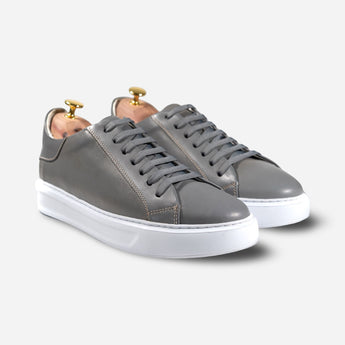 Men's grey leather sneakers with white sole, photographed at an angle showcasing the front and side profile – Shoescoo Elegante model.