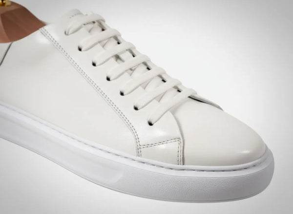 Clean low-top profile of men’s white dress sneakers with sculpted balanced sole — minimalist white leather sneakers for business-casual wear.
